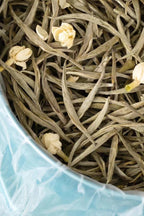 Tea leaves with small white flowers in a blue container